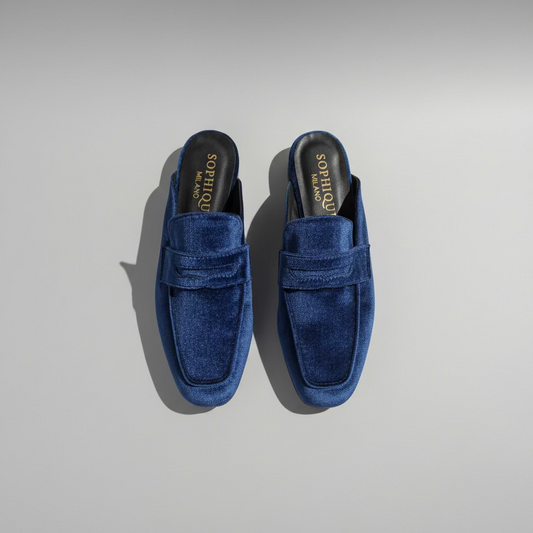 A pair of blue velvet penny loafers with a square toe, displayed on a wooden floor. The brand name 'Sophique Loafers' is visible on the insole.